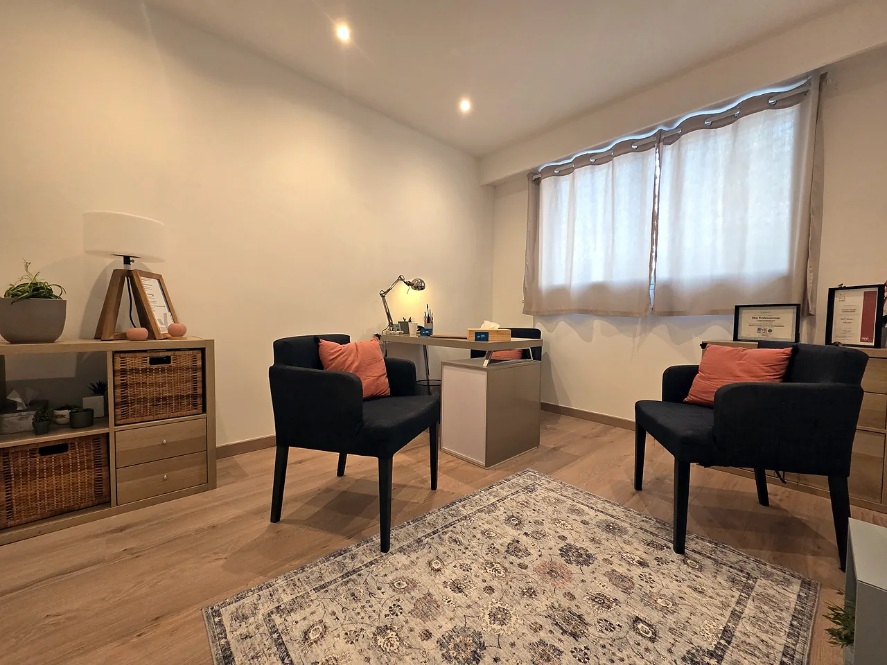 Le bureau de Christel Louvet : deux fauteuils gris à coussins orangés, un tapis et une fenêtre voilée de rideaux clairs